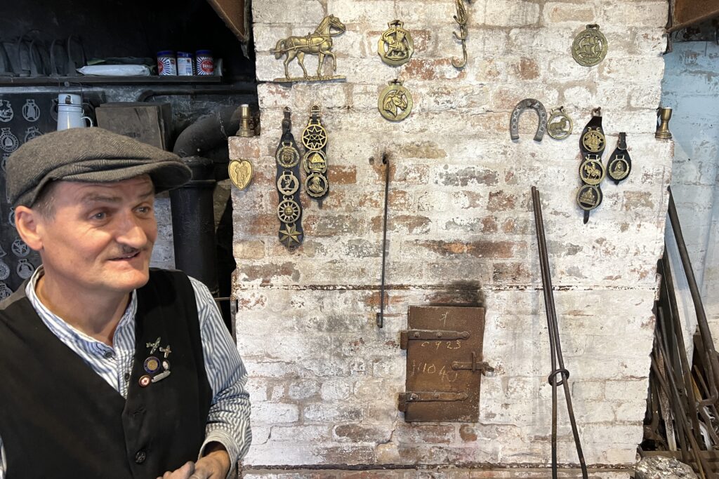 De bronsgieter van het Black Country Living Museum met horse brass op de achtergrond